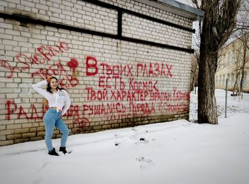 Full length of woman standing on snow against graffiti wall