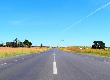 Road passing through field against blue sky