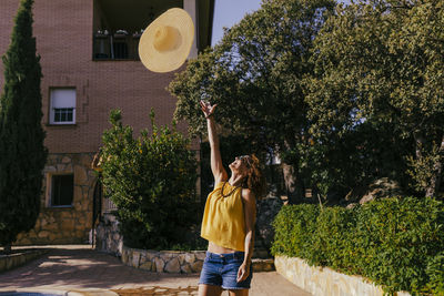 Smiling woman throwing hat while standing against trees