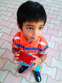 High angle portrait of cute boy holding gift while standing on footpath