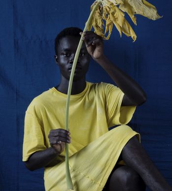 Portrait of woman holding leaf while sitting against curtain