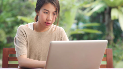 Young woman using mobile phone while sitting on table