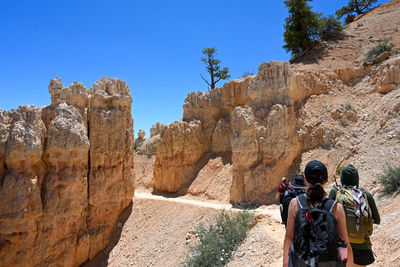 Rear view of woman standing on rock against clear blue sky