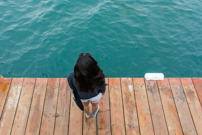 Rear view of woman sitting on pier over sea