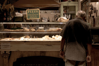 Rear view of a old man buying food in front of the showcase