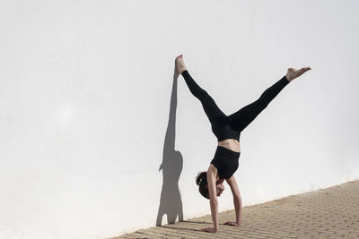 Woman doing a handstand against a white wall in the sun