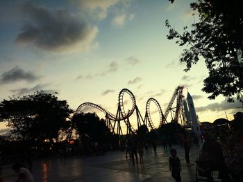 Silhouette people at amusement park against sky