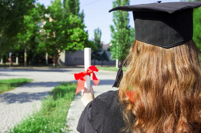 Rear view of woman wearing graduation gown and mortarboard outdoors