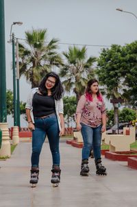 Portrait of smiling young woman with friend skateboarding on footpath in park