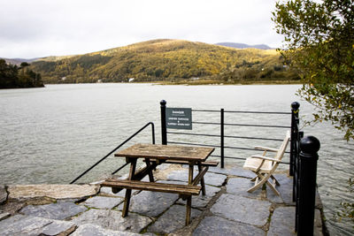 Railing on table by lake against sky