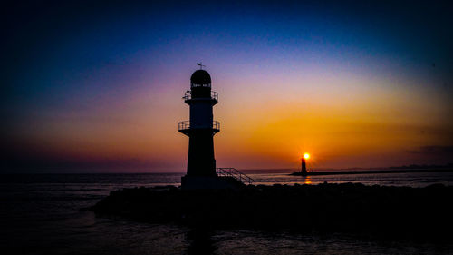 Lighthouse by sea against sky during sunset