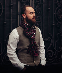 Thoughtful bearded man standing against metal grate