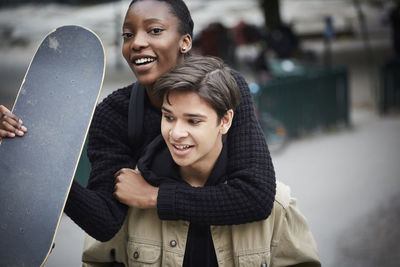 Young man piggybacking female teenage friend with skateboard