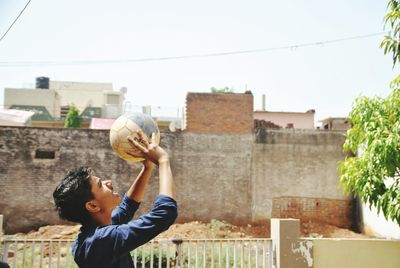 Side view of man holding basketball against building