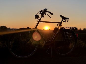 Silhouette bicycle on field against clear sky during sunset