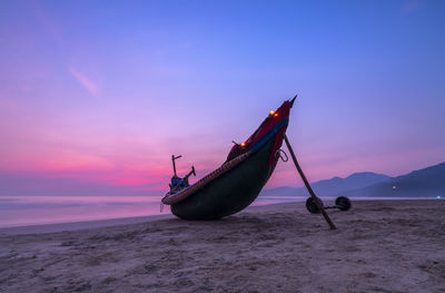 Fishing boat on beach against sky during sunset