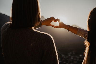 Rear view of couple making heart shape against sky