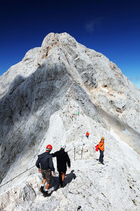 Low angle view of people on mountain against clear blue sky