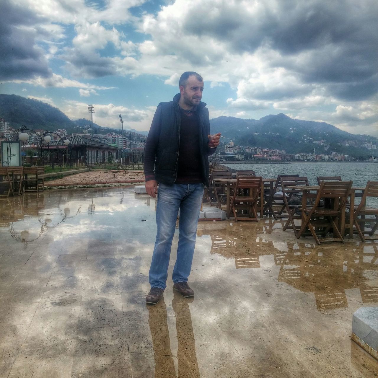 sky, lifestyles, building exterior, casual clothing, built structure, cloud - sky, architecture, standing, water, leisure activity, young adult, full length, person, young men, cloud, cloudy, three quarter length, mountain