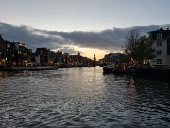 River by buildings against sky at sunset