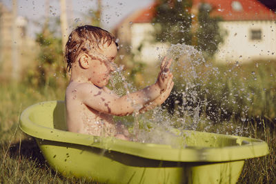 Cute little boy bathing in tub outdoors in garden. happy child is splashing, playing with water 