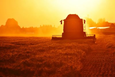 Combine harvester on field against sky during sunset