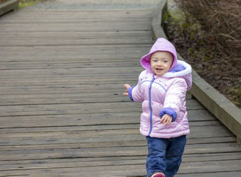 Cute baby girl wearing warm clothing standing on footpath
