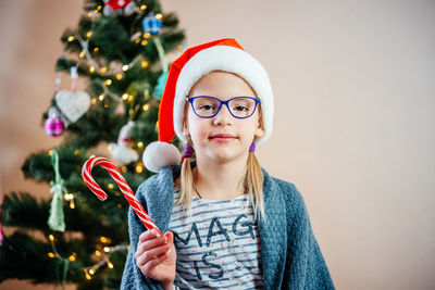 Little girl in eyeglasses and santa hat eating candy cane lollipop lo at christmas time