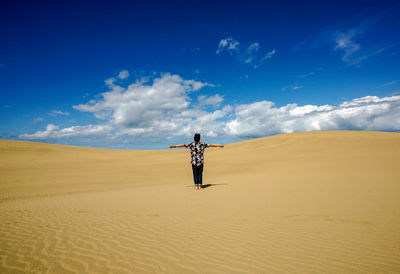 Rear view of man with arms outstretched standing at desert