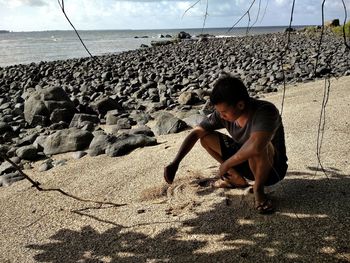 Full length of boy on rock at beach against sky