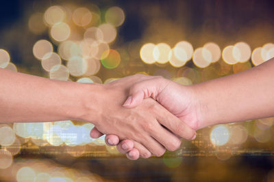 Cropped image of people shaking hands against illuminated lights