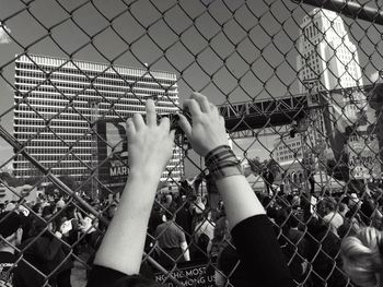 Midsection of woman holding chainlink fence against sky