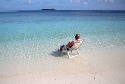 Rear view of man sitting on chair at beach