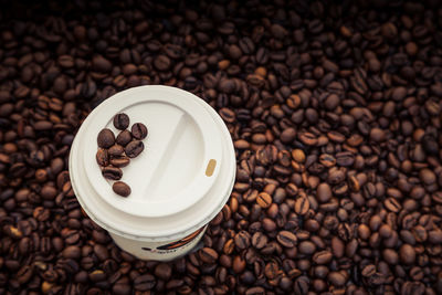 High angle view of disposable cup on roasted coffee beans