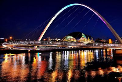 Illuminated bridge over river against sky at night