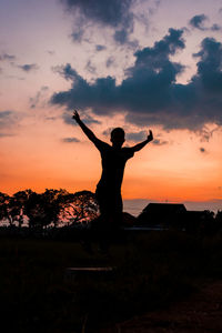 Rear view of man with arms outstretched standing against sky during sunset