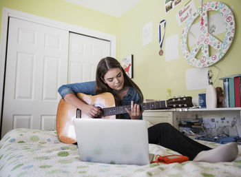 Woman practicing guitar while sitting by laptop at home