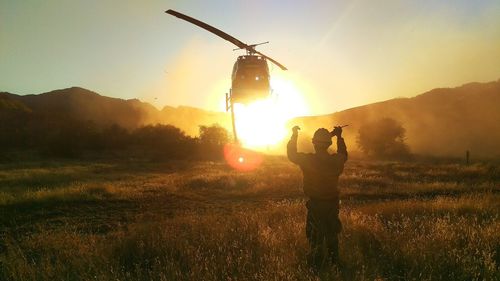Man standing in field against helicopter during sunny day