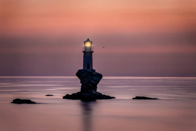 Lighthouse by sea against sky during sunset