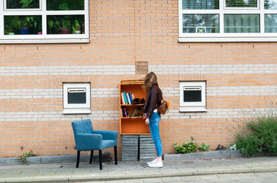 Full length of woman using mobile phone against building