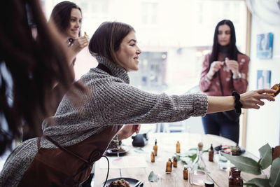 Smiling female owner holding perfume bottle amidst colleagues at workshop