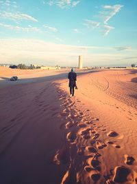 Rear view of woman on dessert against sky during sunset