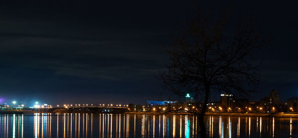 Illuminated city by river against sky at night