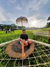 Young man sitting on plants against sky