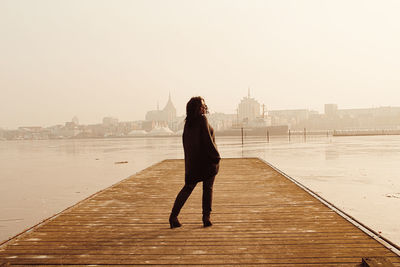 Full length rear view of woman standing on pier over lake against clear sky