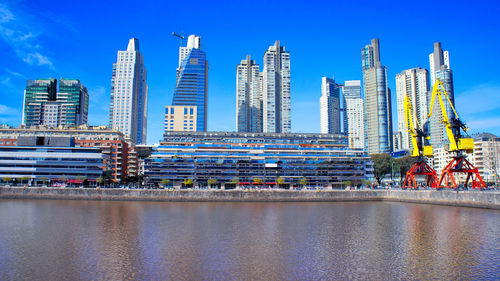 Modern buildings by river against blue sky