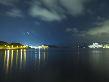 Illuminated city by sea against sky at night