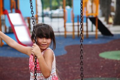 Portrait of smiling girl standing by swing at playground