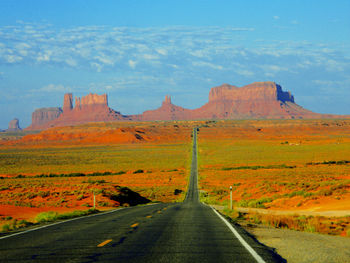 Road leading towards rocky mountains against sky at monument valley