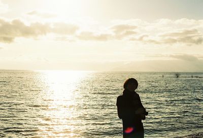 Silhouette man standing in sea against sky during sunset